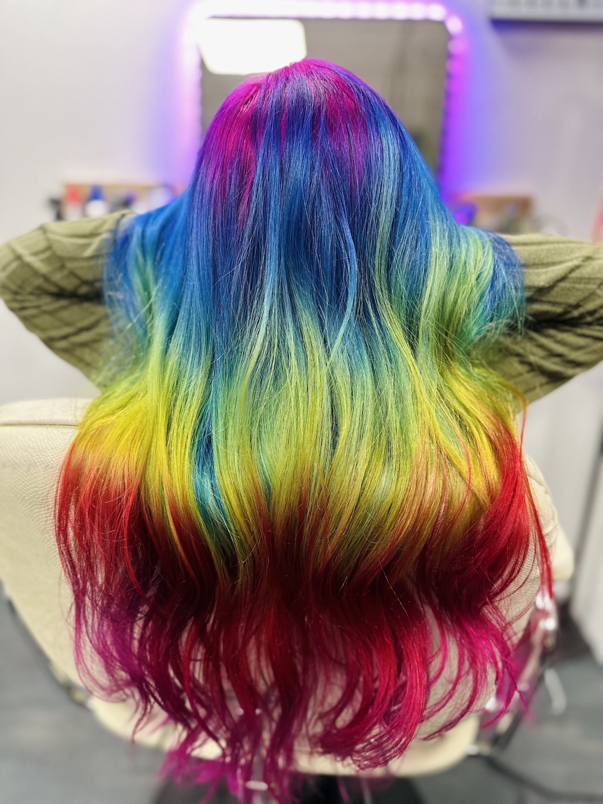 Lang haar in regenboogkleuren, blauw en groen bovenaan, geel en rood in de punten, in de stoel van de salon