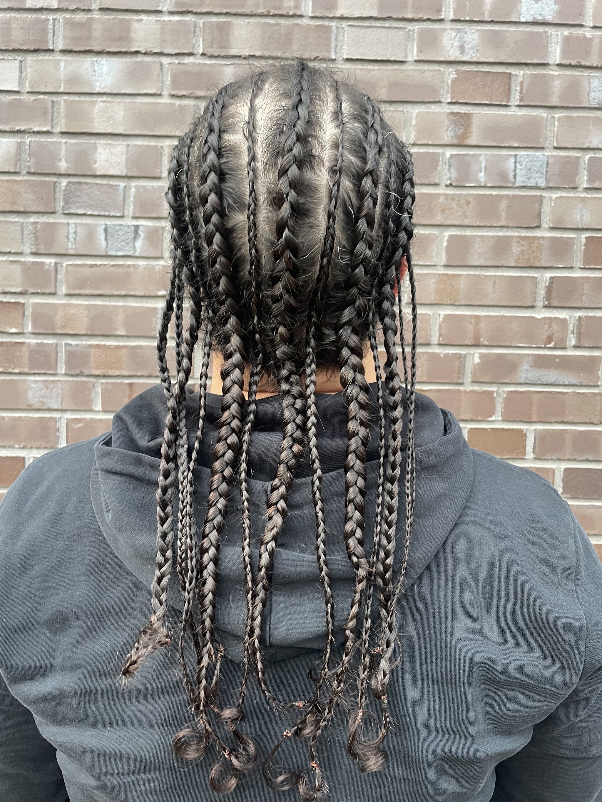 Cornrows die overgaan in lange vlechten, van achteren voor een bakstenen muur