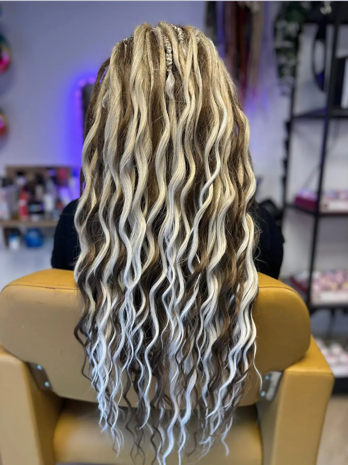 Lange blonde en witte gekrulde dreads in de gele stoel van de salon